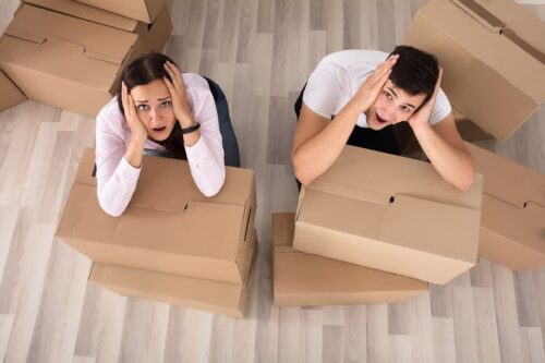 Two people sitting on the floor surrounded by moving boxes, representing the stress MyTee Movers helps reduce with professional packing and unpacking services.