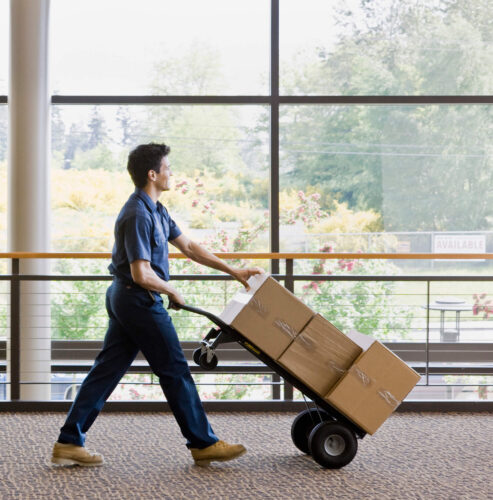 Mover in a blue uniform pushing a hand truck loaded with boxes, representing MyTee Movers’ Loading & Unloading service.